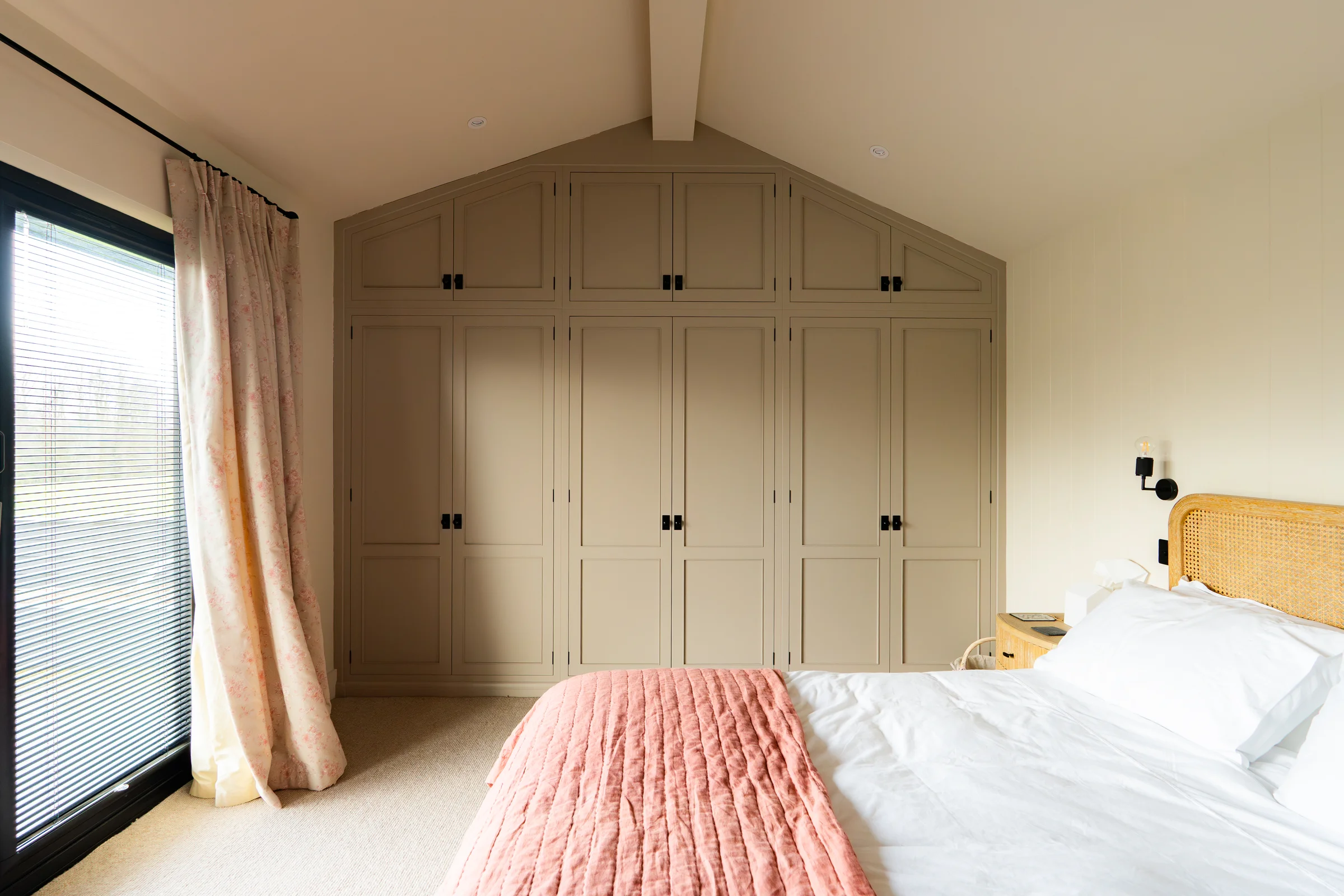 Bedroom taupe fitted wardrobes gable wall black knobs pink throw rattan headboard vaulted