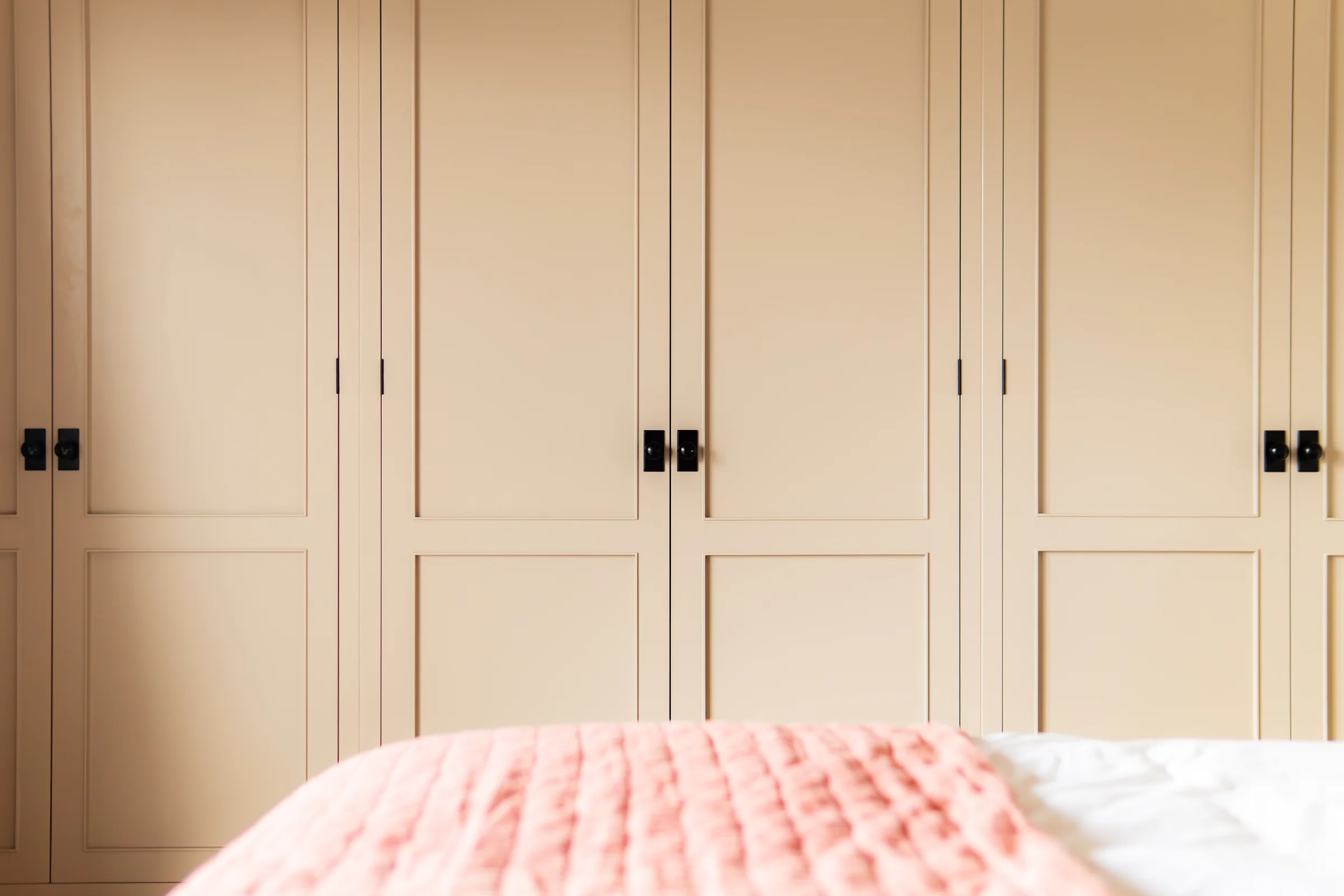 Beige wardrobe doors closeup alt angle black knobs pink throw