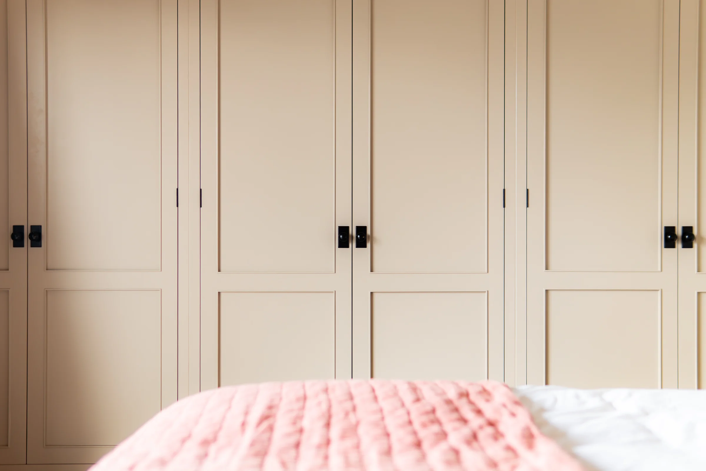 Beige wardrobe doors closeup black square knobs pink throw foreground