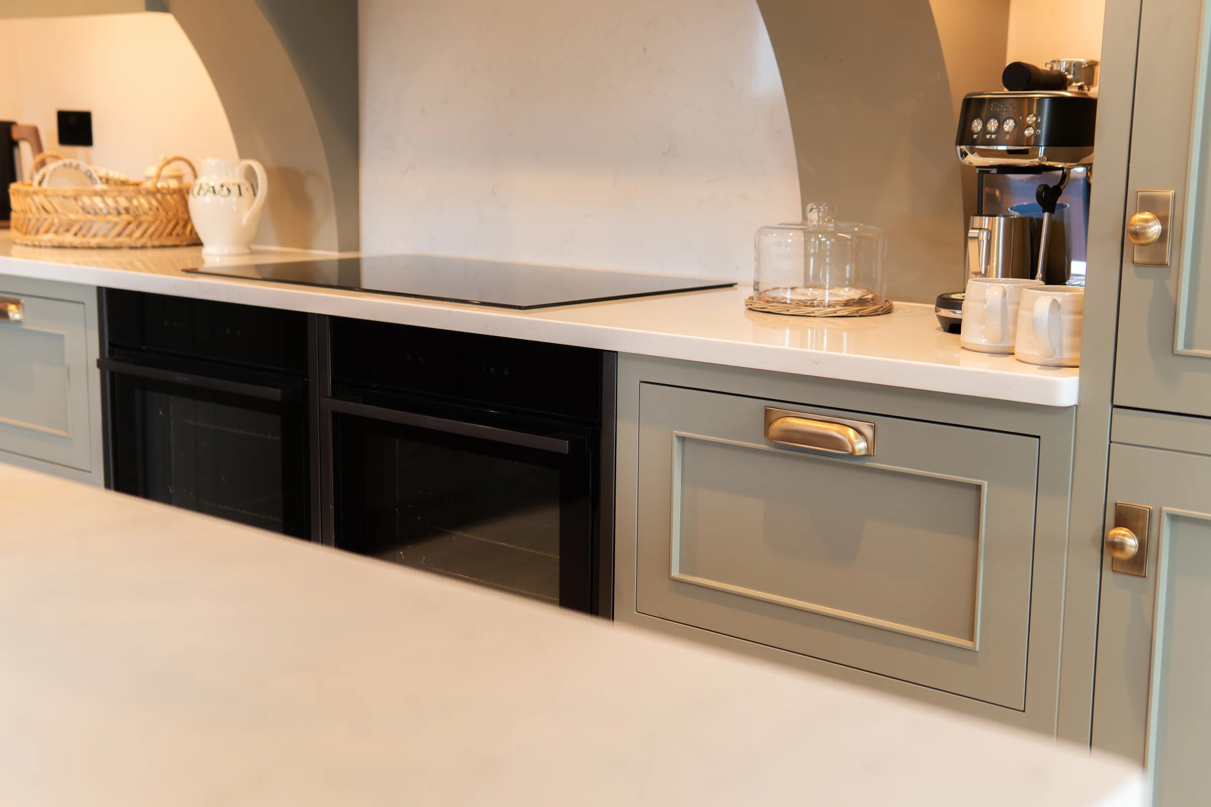 Cooking area closeup hob black ovens grey shaker drawer brass cup handle coffee machine
