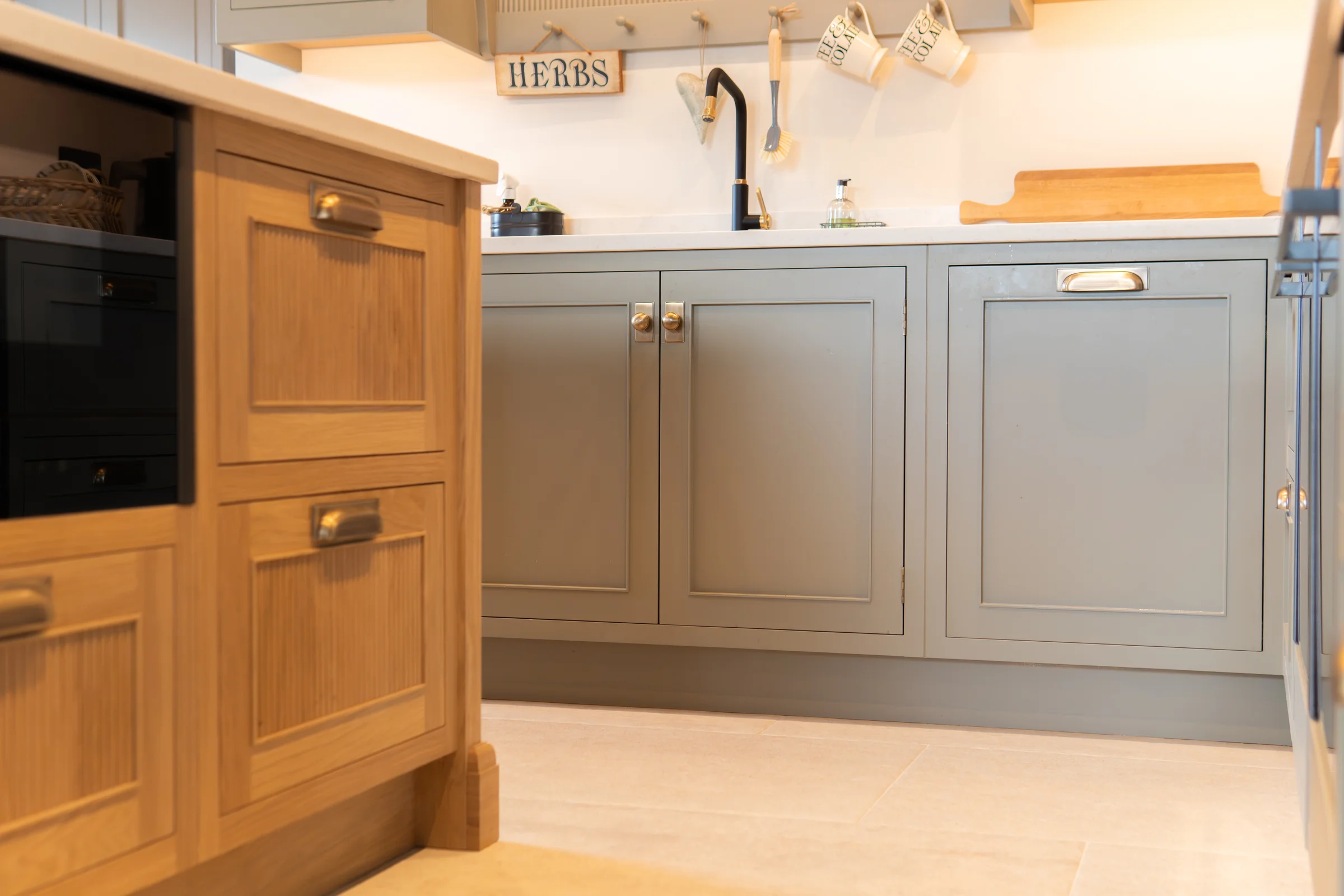 Low angle oak island shaker drawers brass cup handles grey sink units behind stone floor