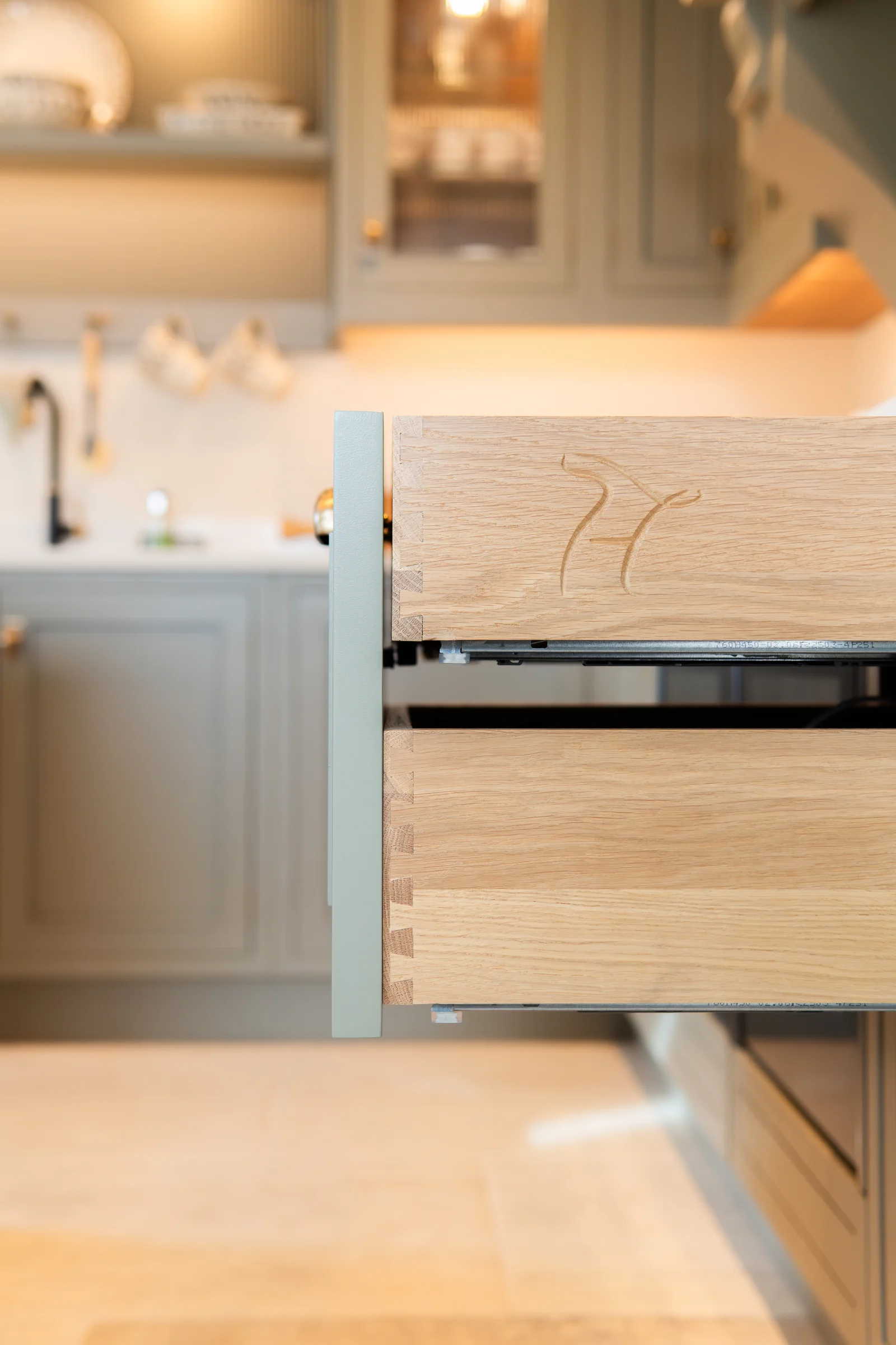 Oak dovetailed drawer side closeup branded h logo engraved joints visible grey behind