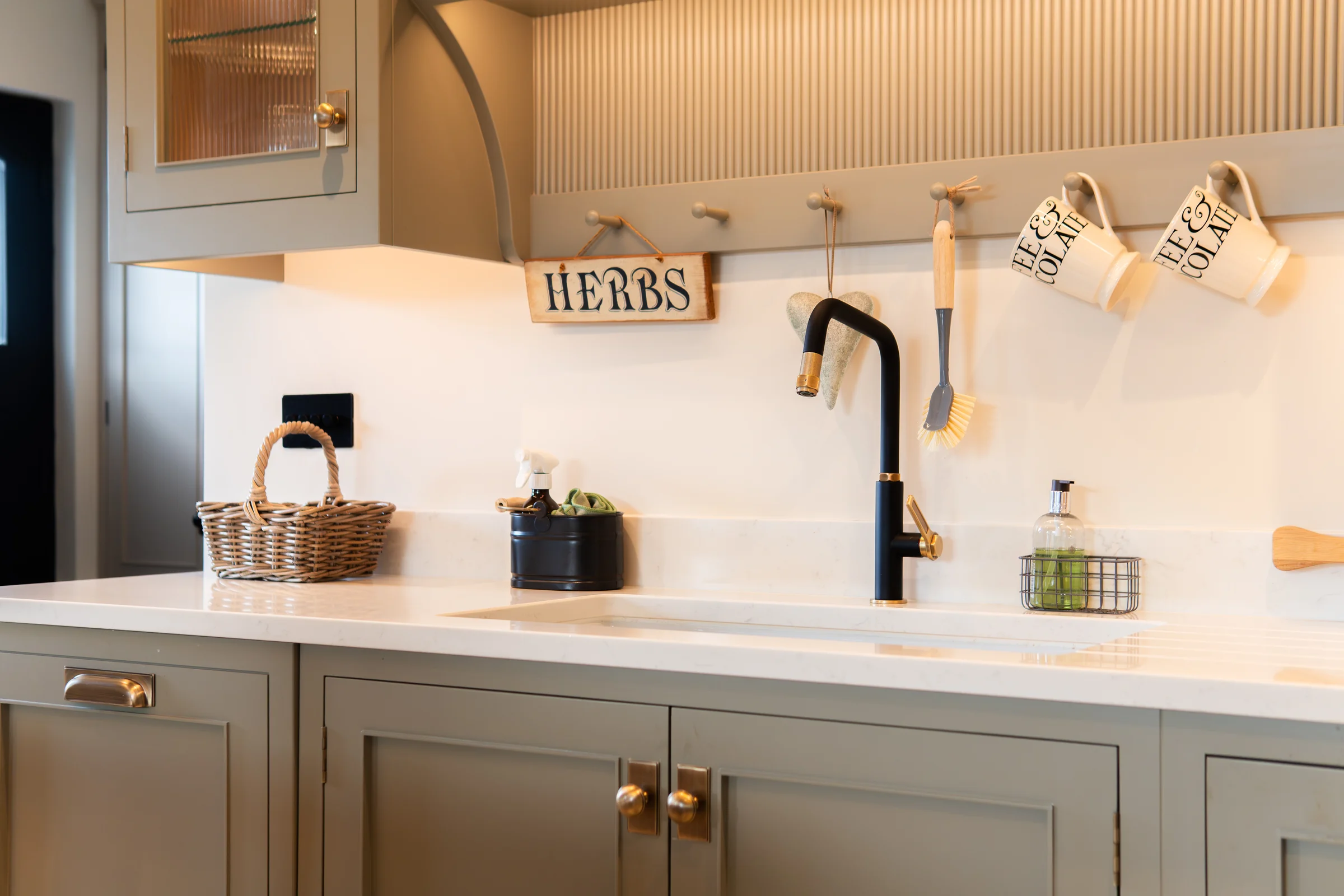 Sink area angle black brass tap grey shaker doors brass knobs quartz herbs sign wicker