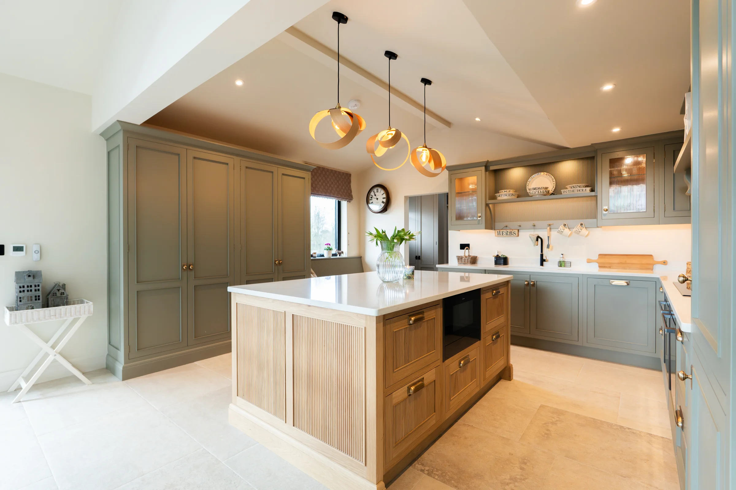 Wide opposite angle oak island built in oven niche brass handles grey tall units pendants