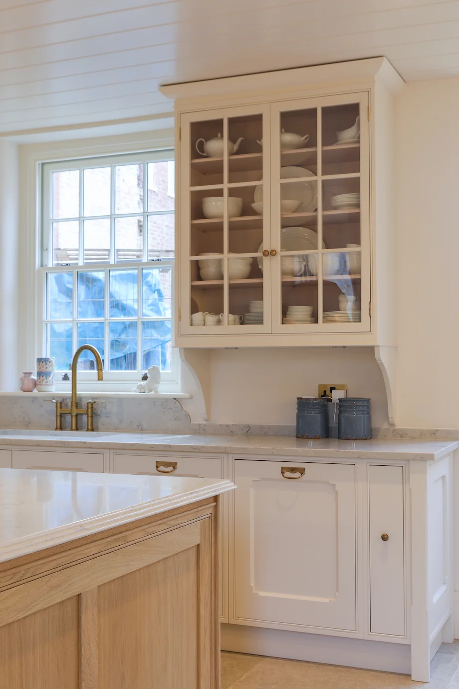 Cream glazed wall cabinet plates bowls brass tap marble worktop
