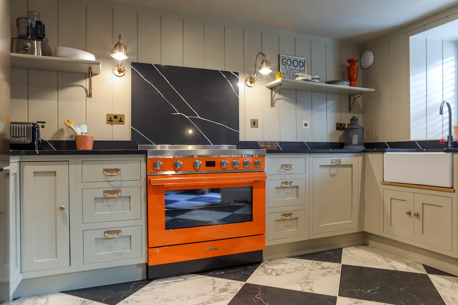 Full kitchen view orange smeg grey units shelves sink panelling marble floor