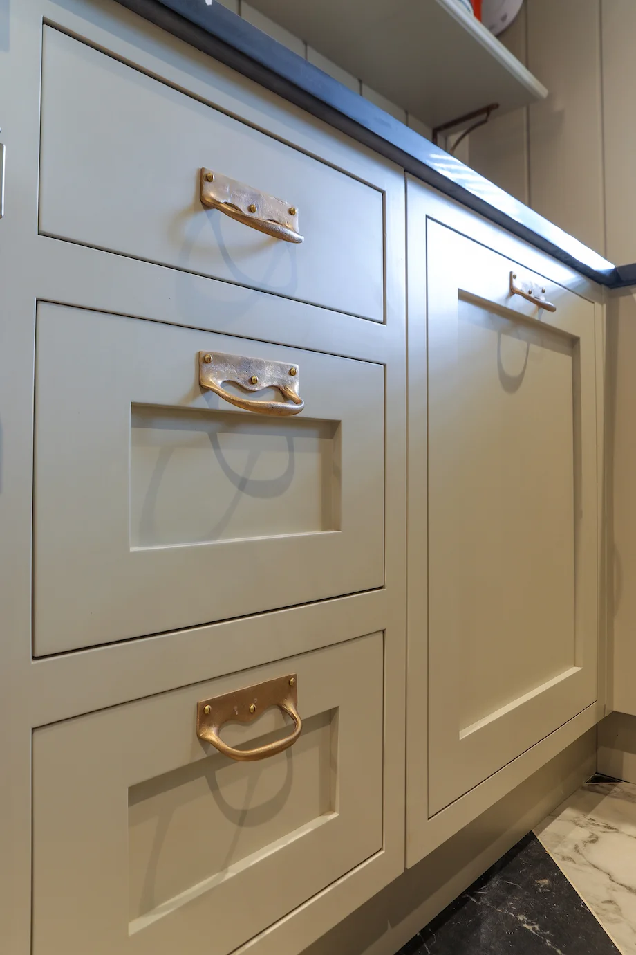 Grey shaker drawer stack closeup brass drop handles three sizes dark quartz
