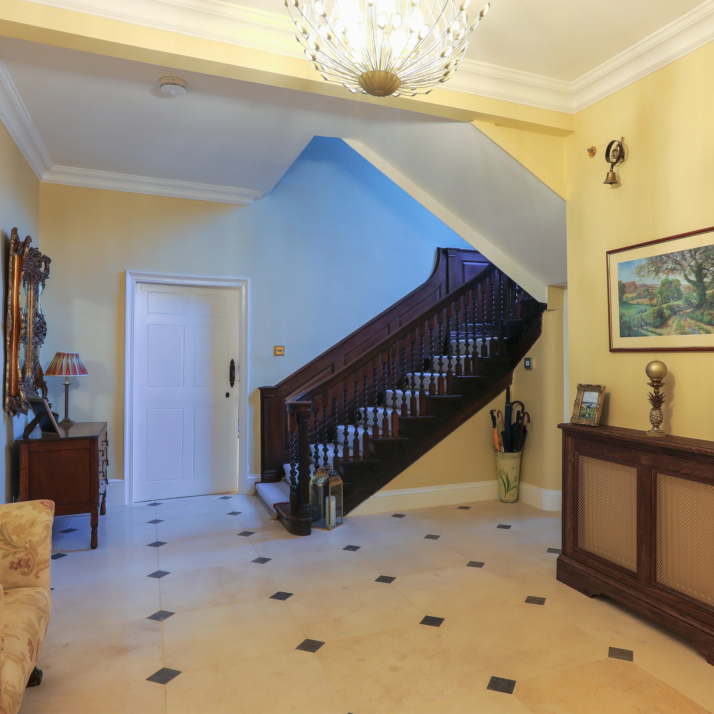 Grand hallway dark wood staircase turned balusters stone floor chandelier radiator cover