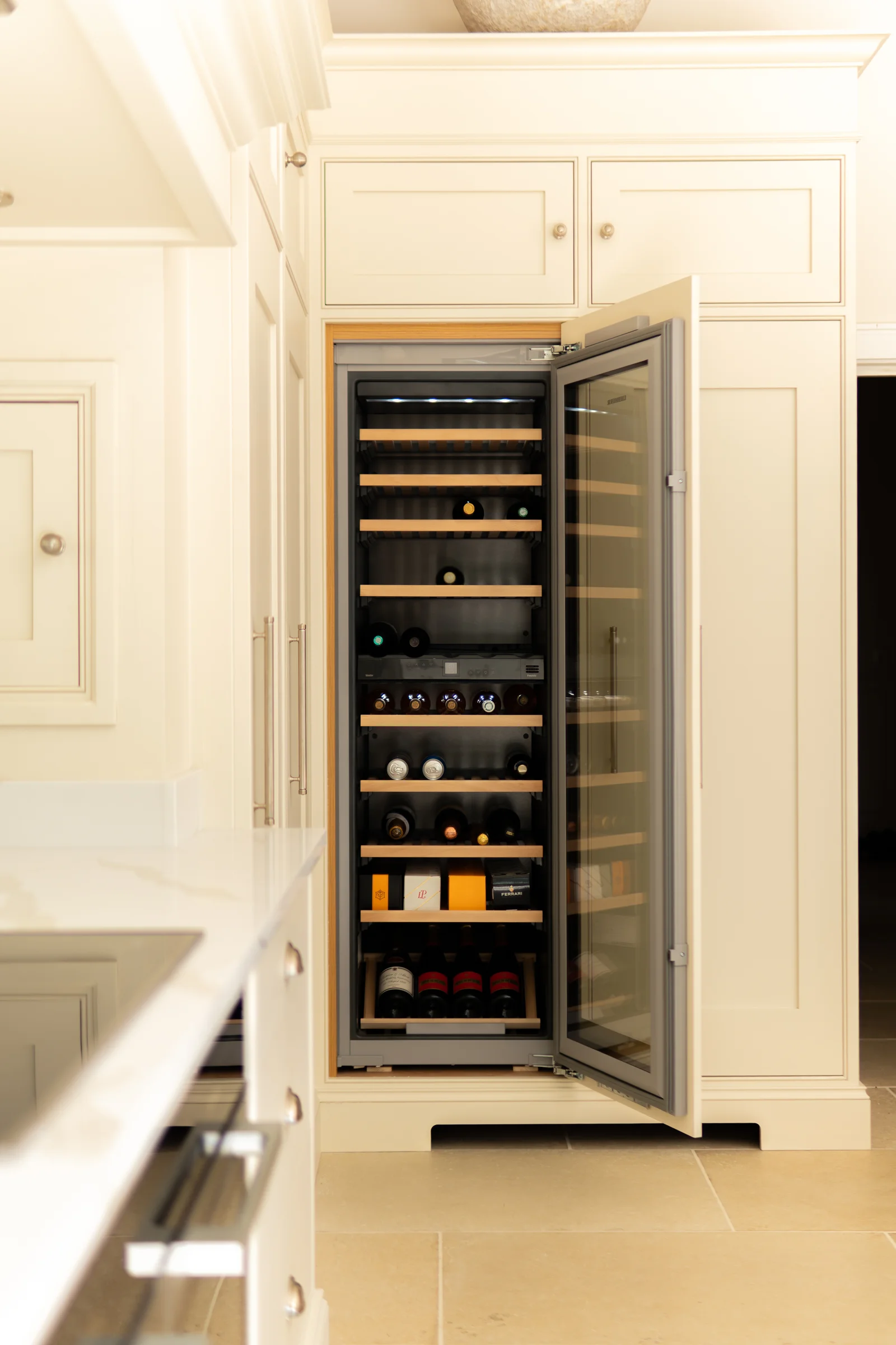 Built in wine cooler glass door oak shelves cream tall cabinetry limestone