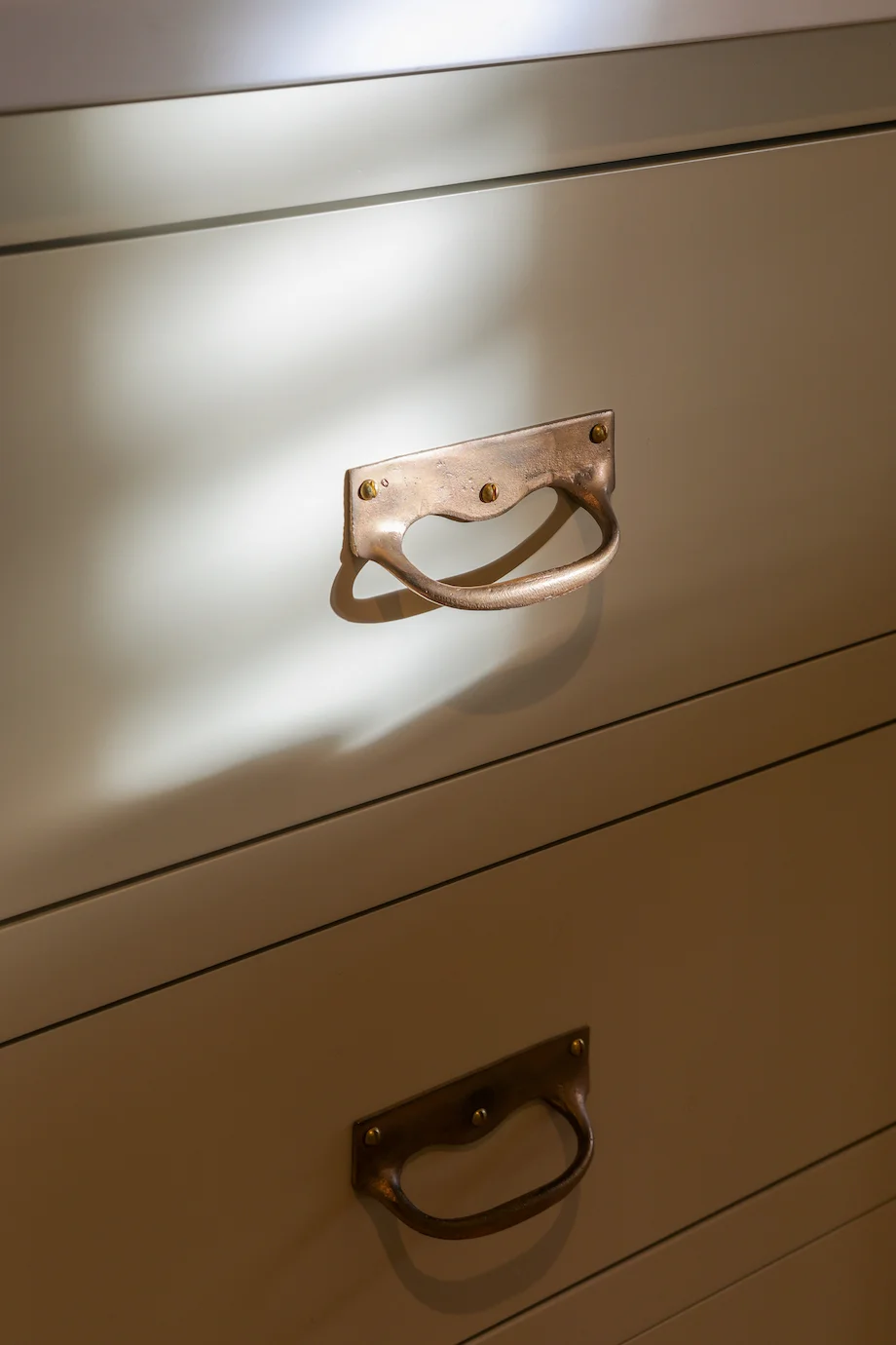 Brass drop handle closeup cream painted drawer sunlight patina detail