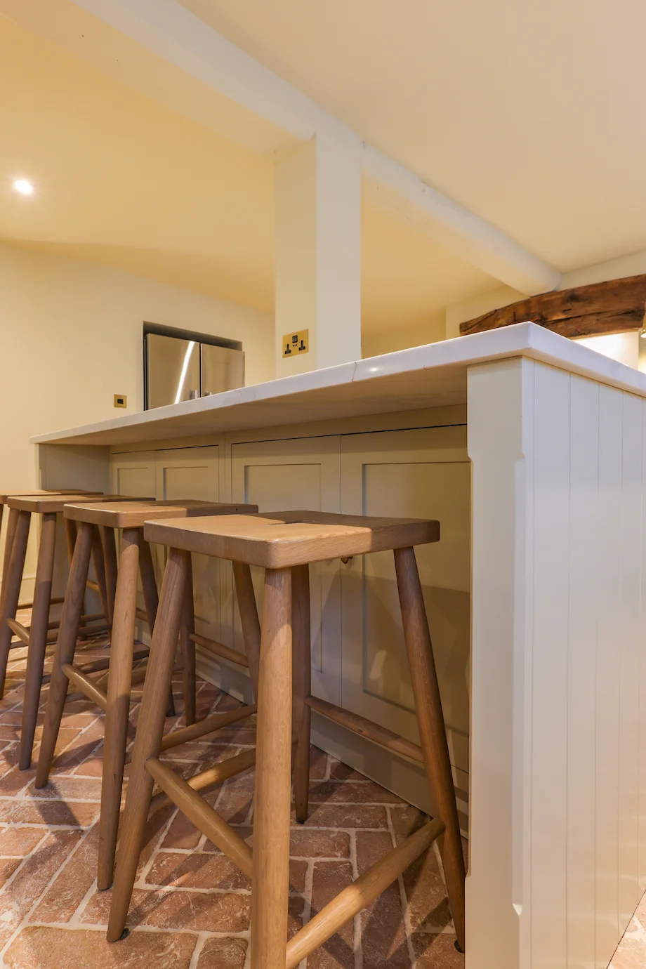 Oak bar stools cream panelled island end quartz worktop brick floor beam
