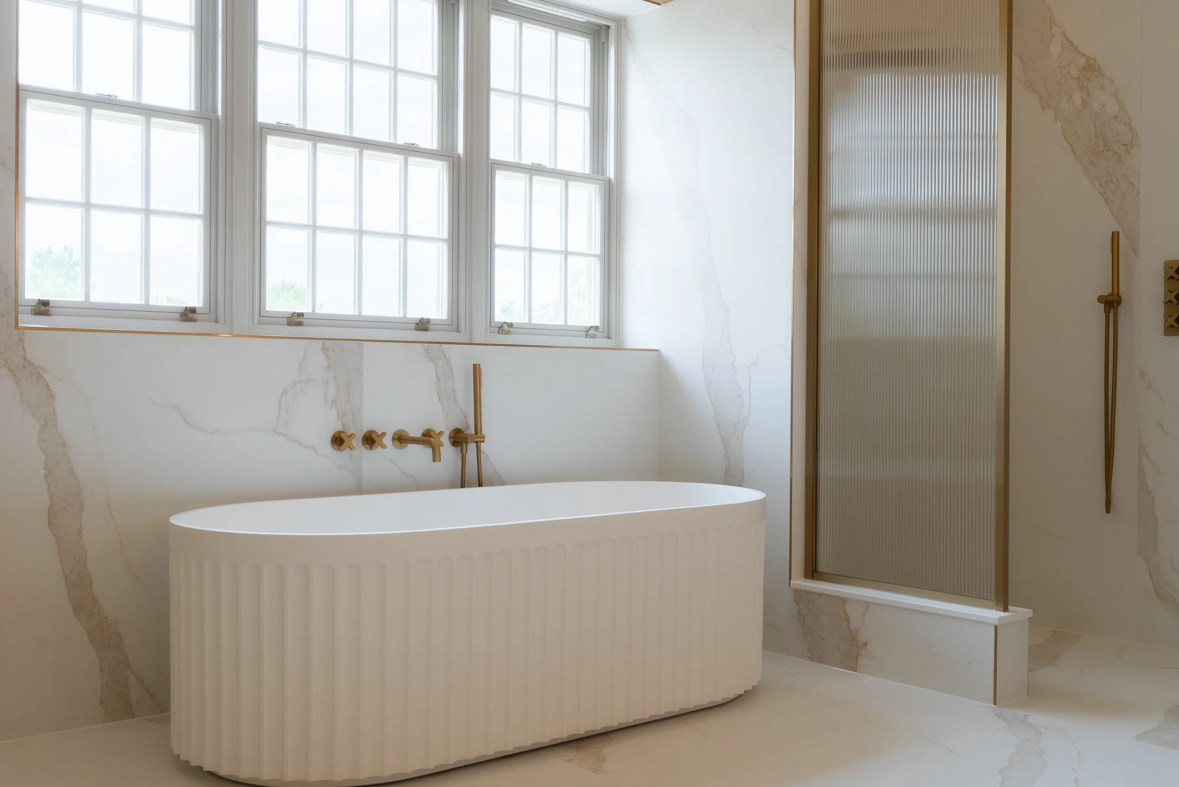 Fluted bath closeup brass wall taps marble walls casement windows reeded glass shower