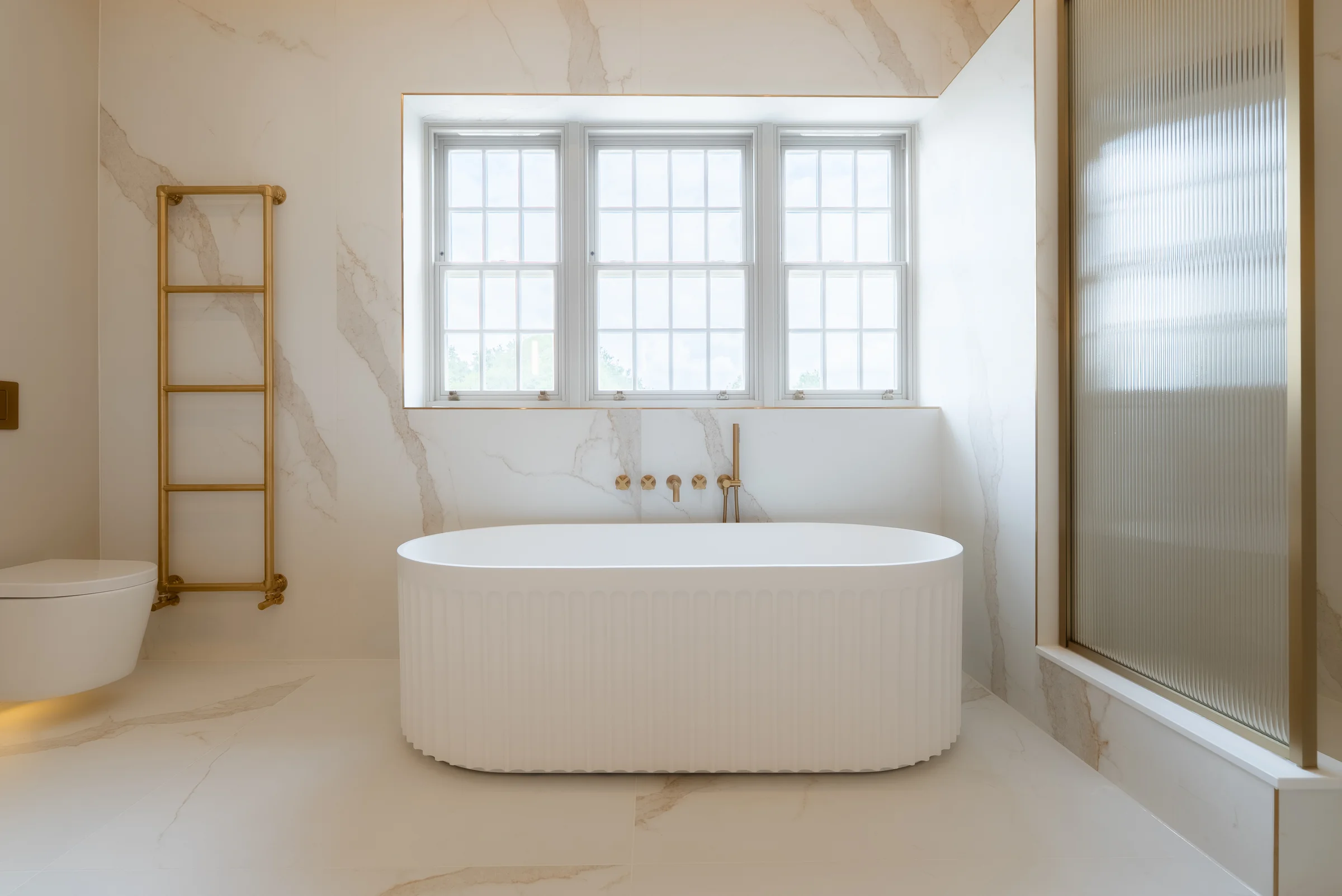 Front on bath fluted freestanding brass taps marble towel rail reeded glass shower