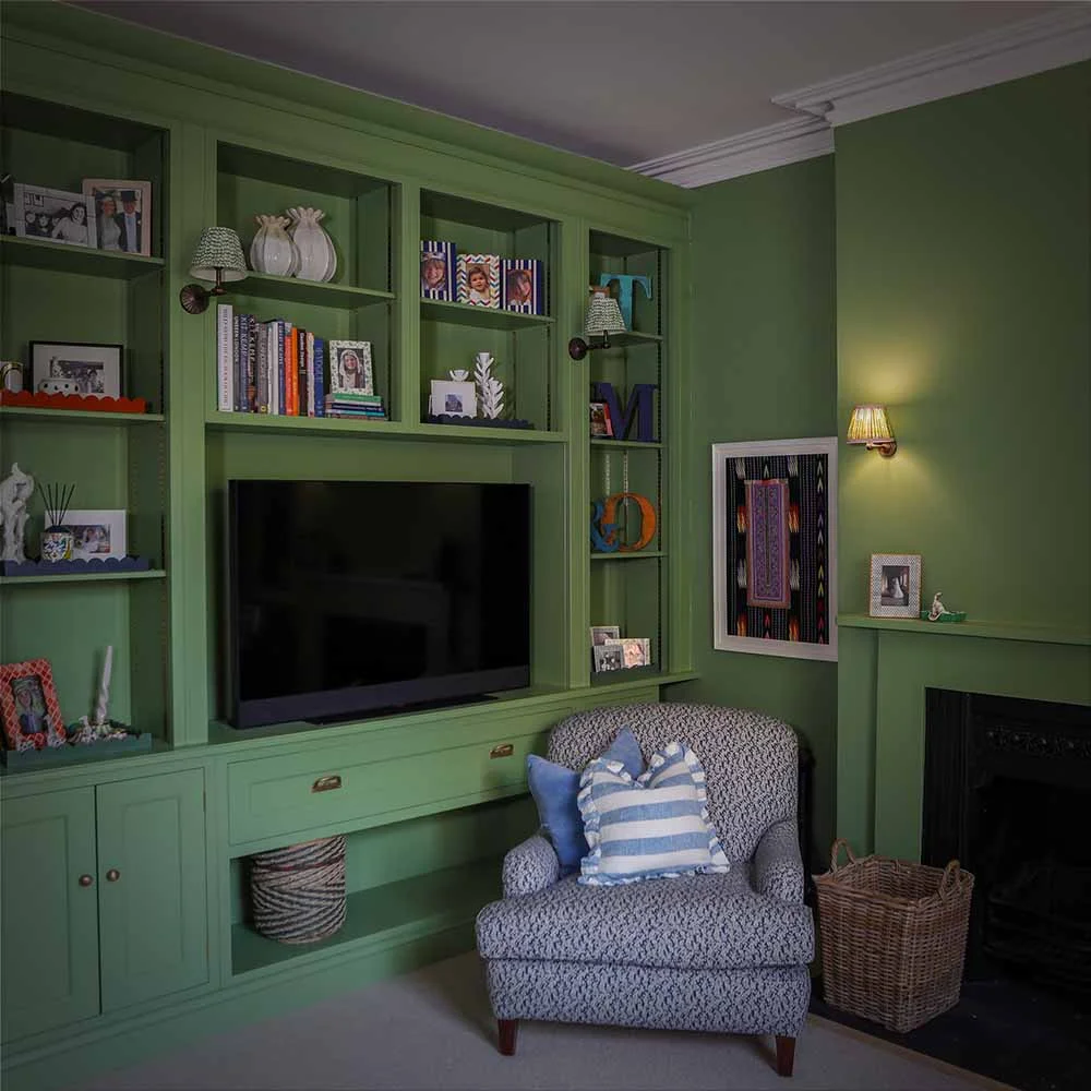 Green painted media cabinet tv unit open shelves books photos brass handles armchair