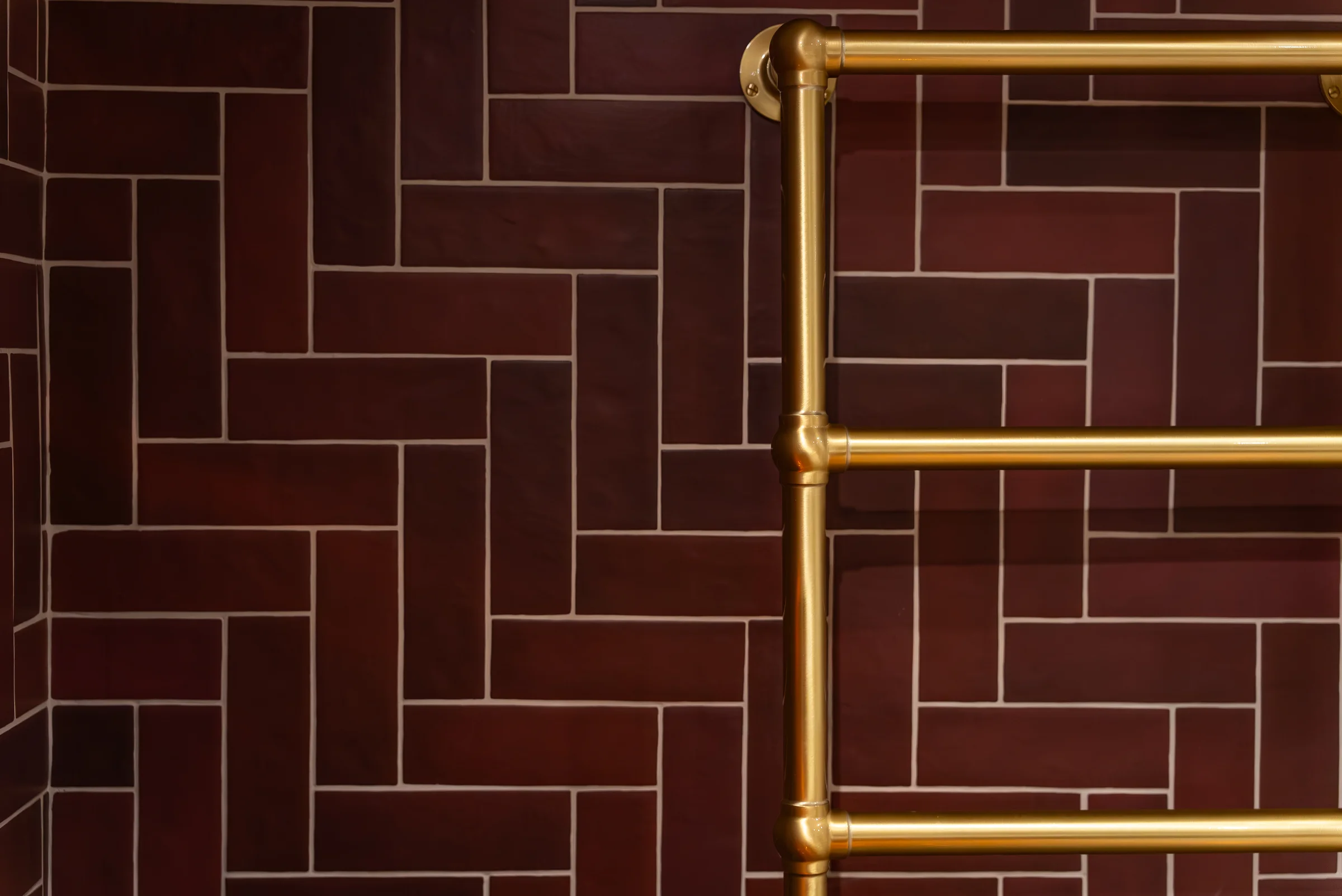 Closeup burgundy herringbone tiles brass towel rail detail