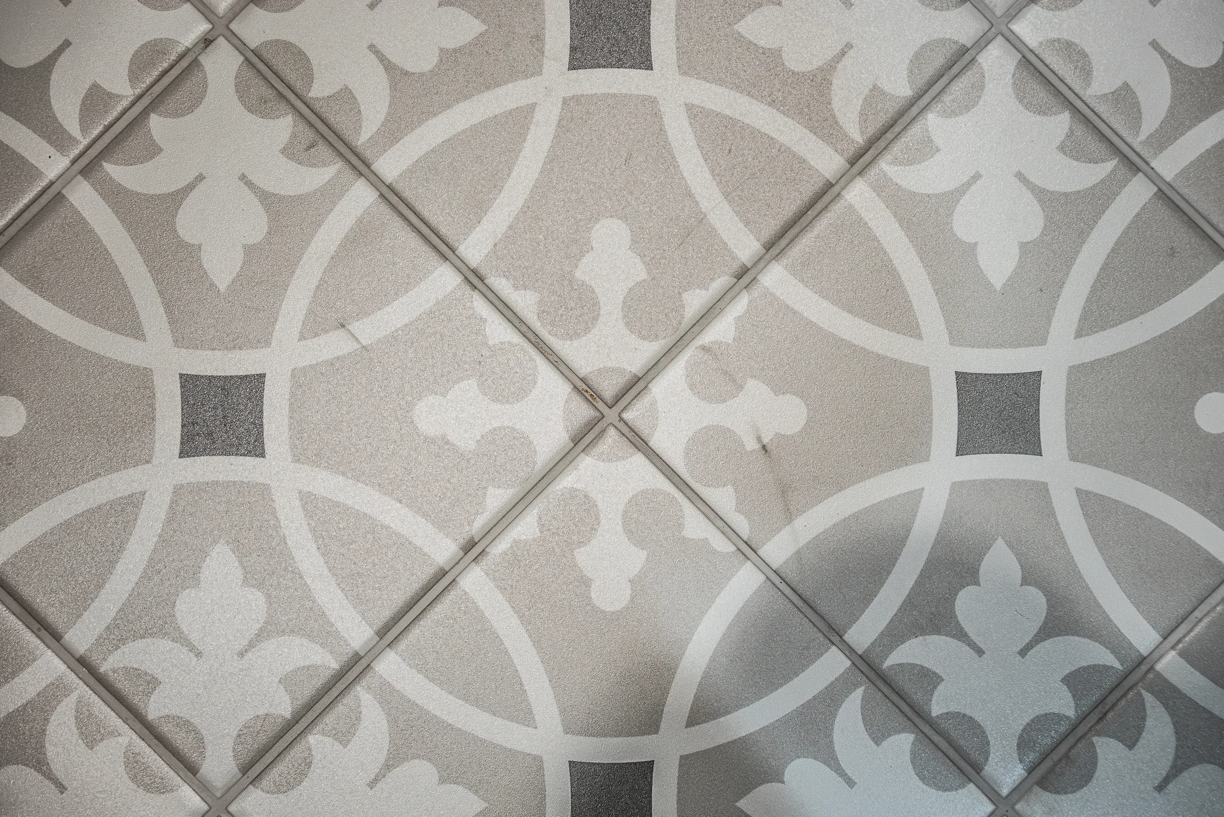 Closeup ornate patterned floor tile grey white fleur de lis motif