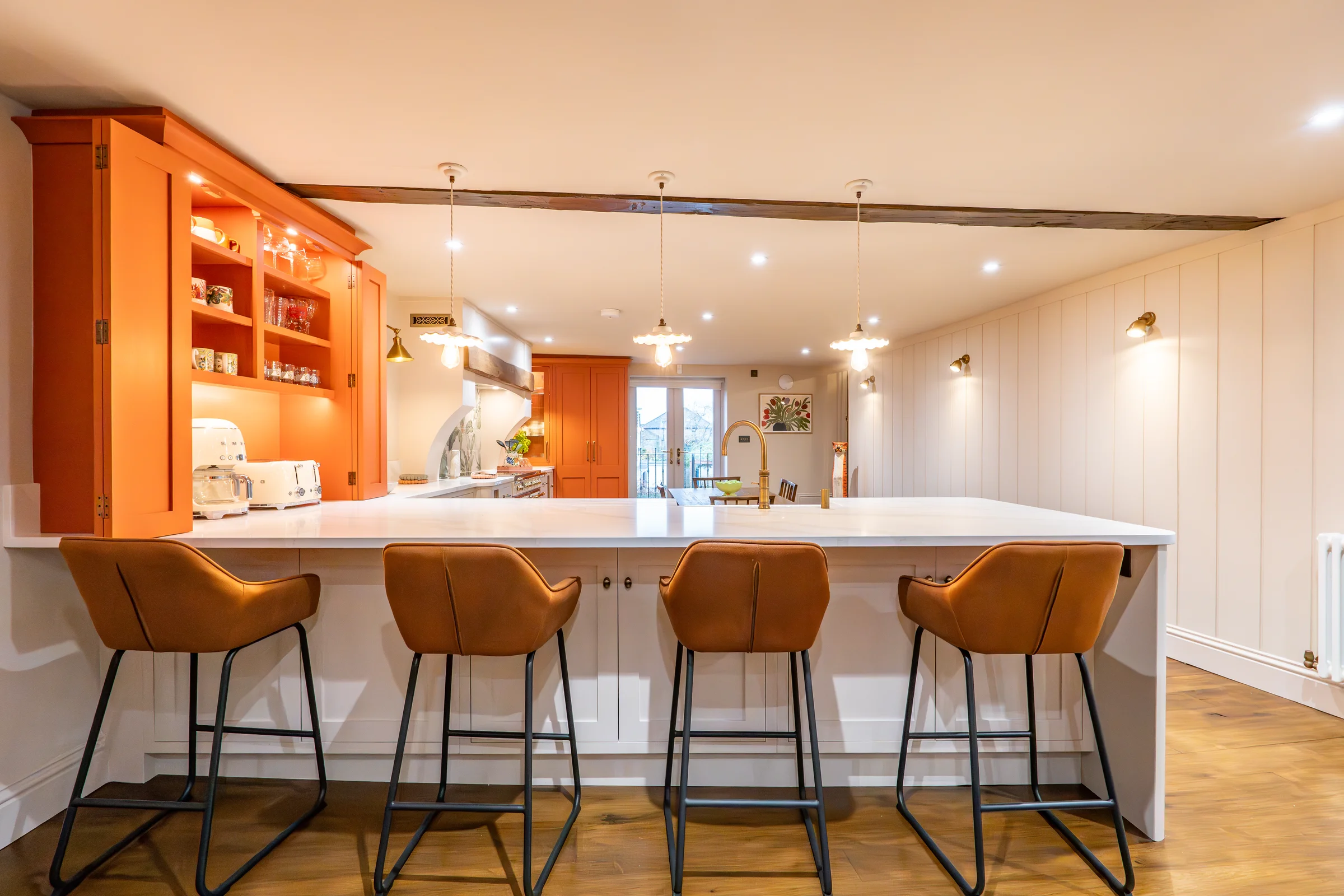 Island opposite angle tan stools orange dresser open shelves pendants beam panelling