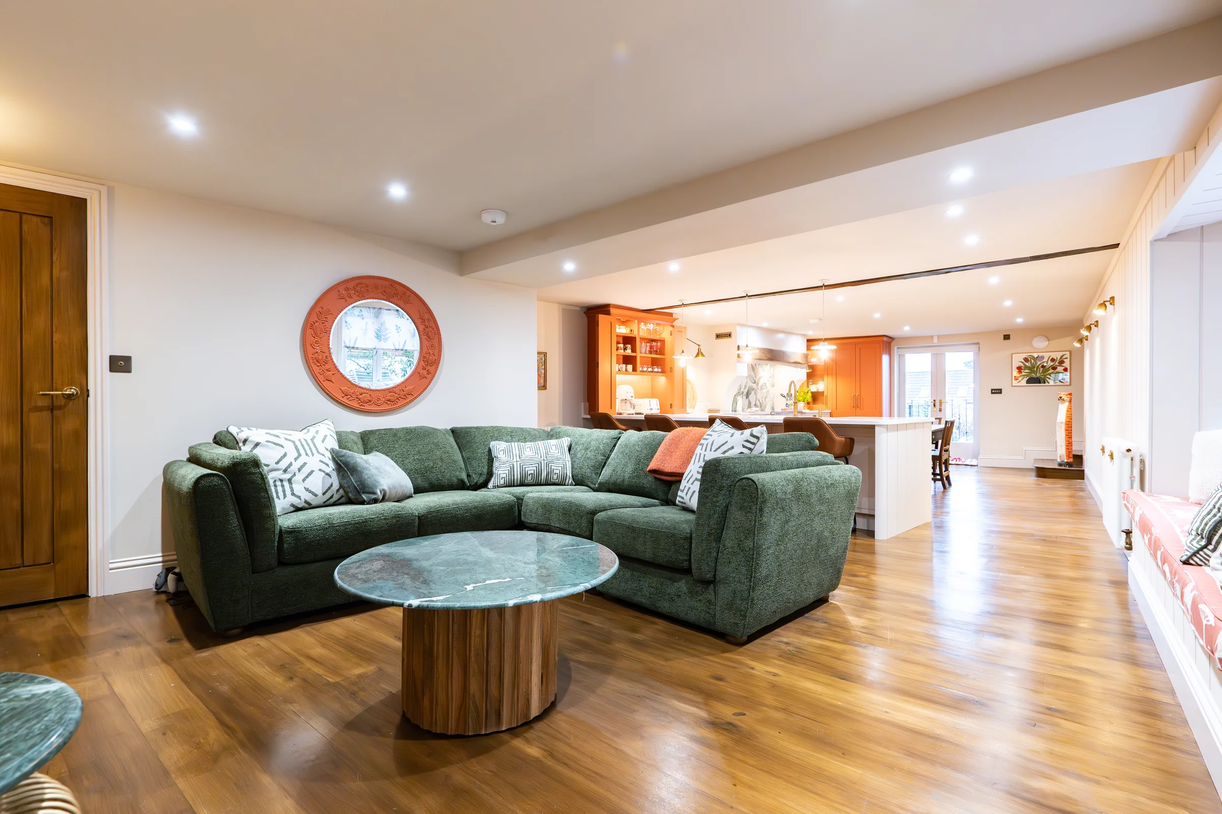 Living area green corner sofa porthole mirror walnut coffee table open plan kitchen