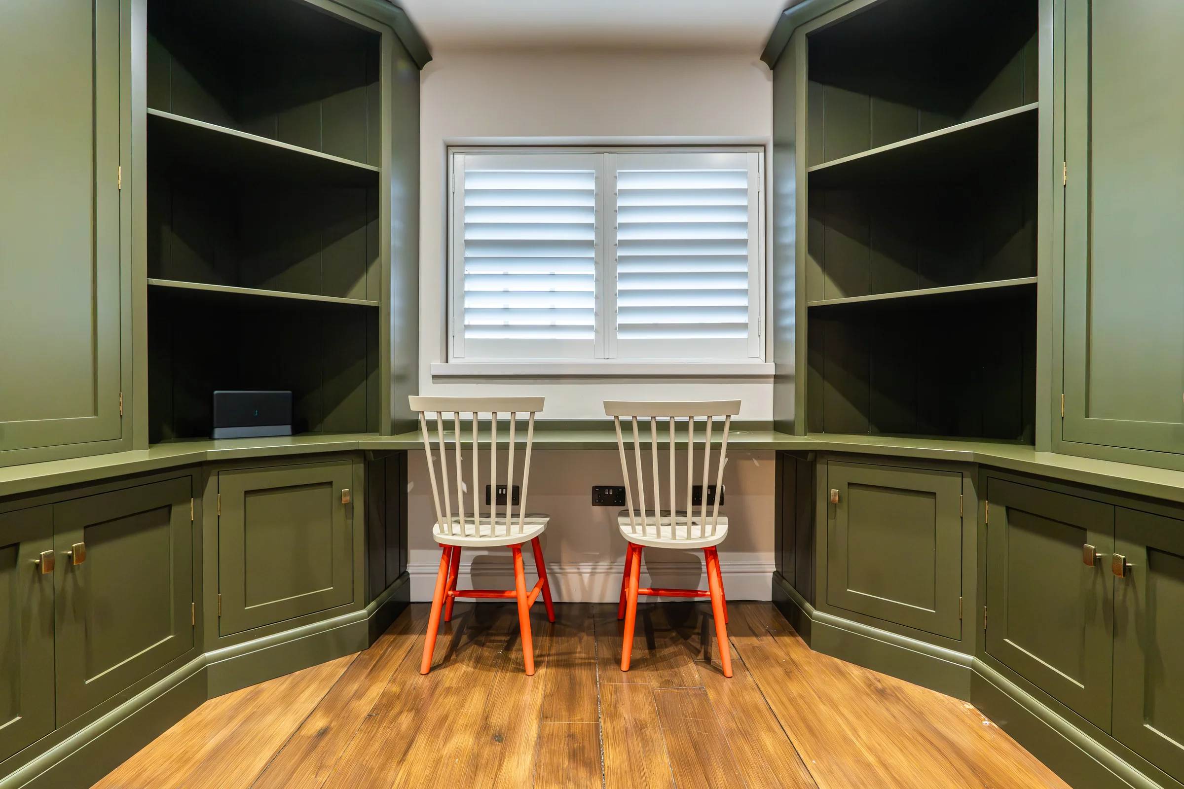 Olive green study built in bookshelves cupboards shutters white chairs orange legs